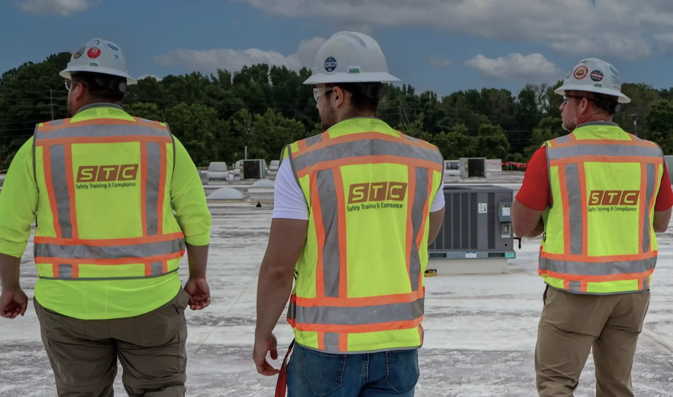 Three men in STC-branded vests and white hard hats survey a work site for safety.