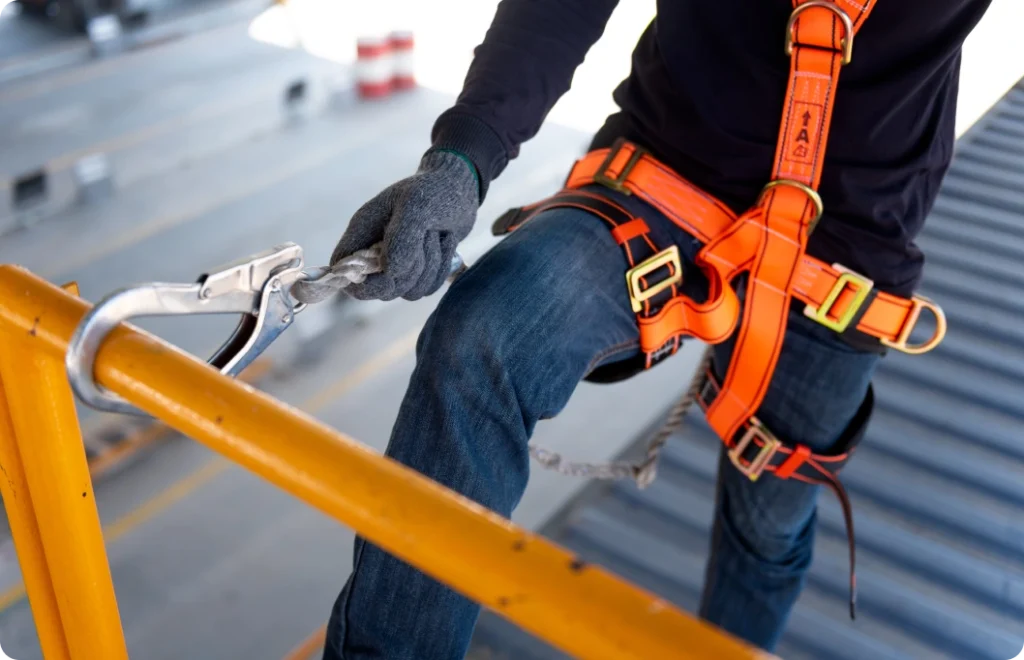 Close-up of a person in jeans and an orange safety harness clipping onto equipment.