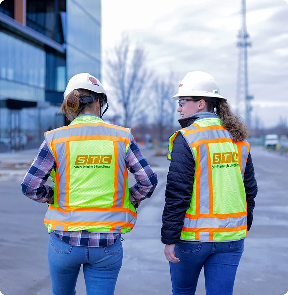 Two women in STC safety vests and hard hats walk towards an office building.